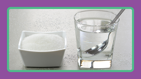 A bowl of sugar sitting next to a glass of water with a spoon.