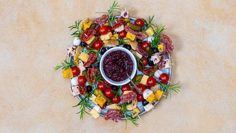 The charcuterie board with embellishments on it and a dip in the bowl in the middle of the plate creating a wreath formation