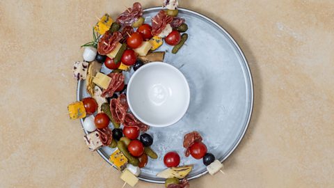 Cocktail sticks with charcuterie being placed on a plate with a small bowl in the middle 