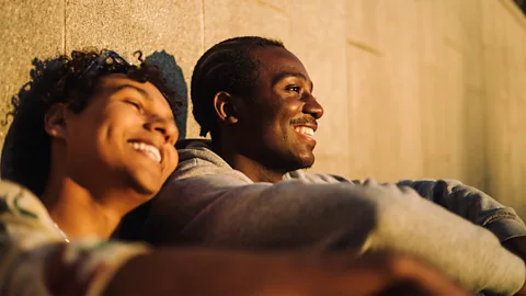 Woman and man smiling leant against wall (Credit: Getty Images)