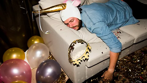 A man sleeping on a sofa, surrounded by the debris from a night of partying  (Credit: Getty Images)