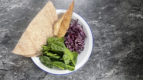 The wrap ingredients in a bowl: One wrap, smoked mackerel, red cabbage and spinach