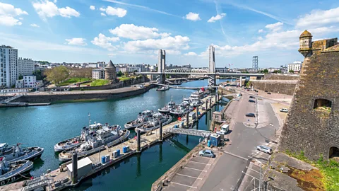 Small boats in Brest harbour, lined up by a jetty. a suspension bridge can be seen in the background (Credit: Getty Images)