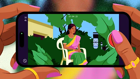 A brightly coloured illustration of a woman's hands holding a smartphone, which shows a woman wearing a green, pink and yellow sari sat on a white chair surrounded by greenery on the screen (Credit: Estudio Santa Rita)