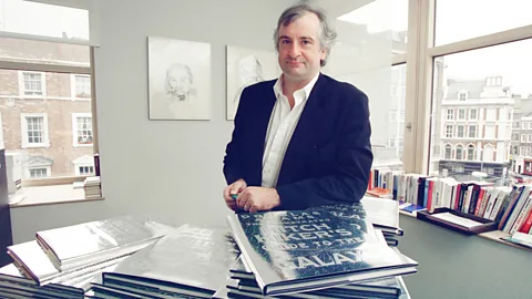 Douglas Adams poses by windows with copies of The Hitchhiker's Guide to the Galaxy in front of him (Credit: Getty Images)