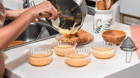 Custard being poured from into four glass bowls on a counter, with baking supplies around them (Credit: Alamy)