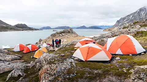 People camping in tents in Greenland, with the ocean and hills in the background (Credit: Alamy)