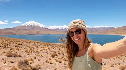 A woman traveller poses for a selfie in front of a mountain and lake (Credit: Getty Images))