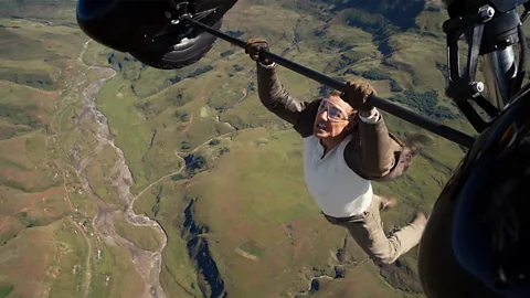 A still of Tom Cruise hanging from a plane with land beneath him in Mission: Impossible – The Final Reckoning (Credit: Courtesy of Cannes FIlm Festival)