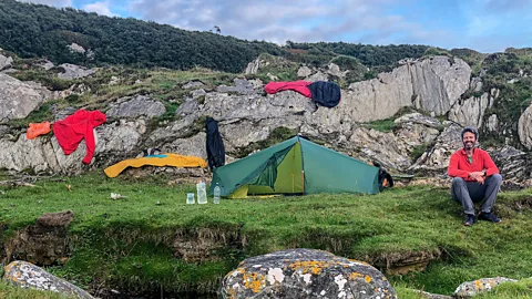 Photographer Quintin Lake sitting outside tent on cliff with clothes hanging on rocks (Credit: Quintin Lake)