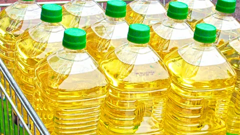A person walking through a shop carrying two big bottles of different seed oils in each hand (Credit: Getty Images)