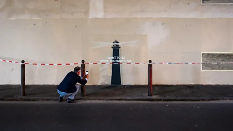 A man taking a photo of Banksy's new mural Lighthouse in Marseille, with text that reads "I want to be what you saw in me" (Credit: Photo of Lighthouse, 2025/ Alamy)