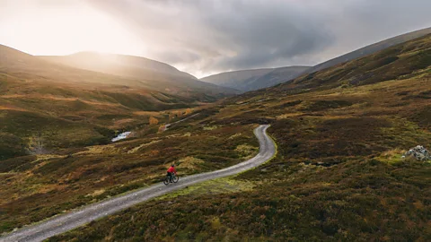 A cyclist riding down a road in the Scottish wilderness (Credit: Getty Images)