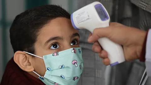 A young girl in a green facemask decorated with mushrooms has her temperature taken using a handheld thermometer (Credit: Getty Images)