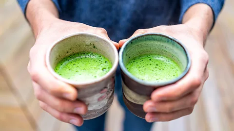 Closeup of hands holding two cups of green matcha (Credit: Alamy)