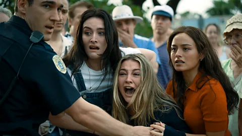 Sarah Pidgeon, Madelyn Cline and Chase Sui Wonders in I Know What You Did Look Summer, being held back by a policeman (Credit: Brook Rushton)