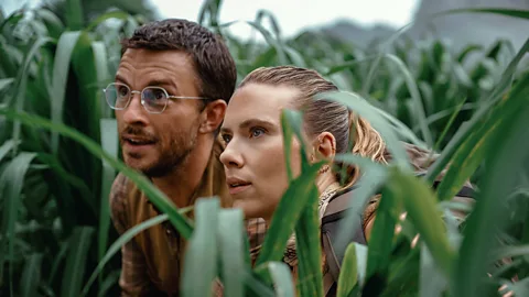 A still of Jonathan Bailey and Scarlett Johansson in the middle of long grass in Jurassic World Rebirth (Credit: Universal Studios)