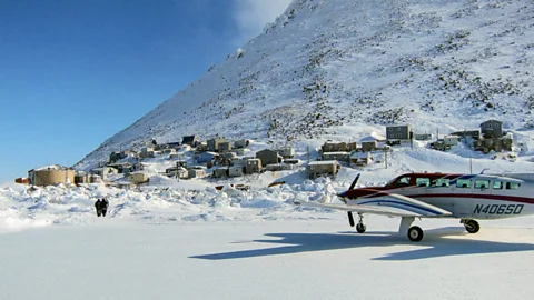 A small plane on Little Diomede with a snow-capped hill and buildings behind (Credit: Matthew Guiffré/ KNOM)