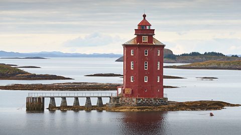 Kjeungskaer Lighthouse on top of a small islet next to a pier - it is red, has three stories and is octagonal in shape 