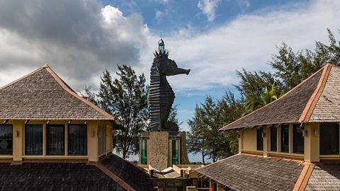 A large bronze sculpture of a seahorses with lighthouse style tip attached on top, it extends above the nearby roof tops
