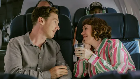Olivia Colman and Benedict Cumberbatch looking at each other while sat on a plane in The Roses (Credit: Searchlight Pictures)