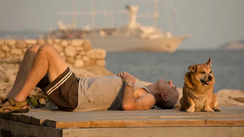 Man lying on wooden platform with small dog with ocean and ship in background (Credit: Ivan Vukoviu0107)