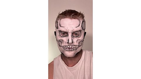 Man with white painted face plus black lines and grey shawdowing painted to look like a skull