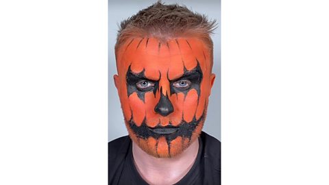 Man with orange painted face plus black shadows around the eyes and mouth