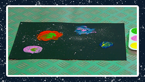 A piece of black card with different coloured shapes of paint on.