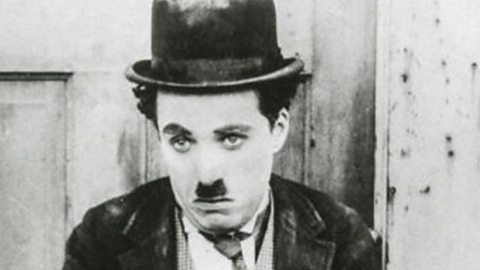Black and white still from a film sees Charlie Chaplin looking sad wearing a dusty bowler hat with a square, thick dark moustache