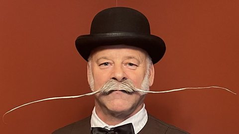 Paul Solsar wears a black bowler hat, shirt and bow tie plus a very long, grey-haired moustache