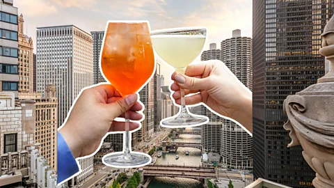 A view of the cityscape of Chicago from a rooftop, with two hands clinking glasses with cocktails (Credit: Amy Ulivieri/ NoMi Garden/ Yun Sun Park)