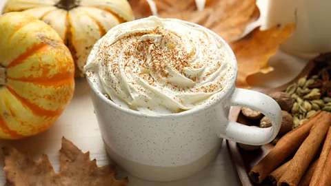 A mug of pumpkin spice latte, with autumnal decorations of mini squash, cinnamon sticks and autumn leaves around it (Credit: Alamy)