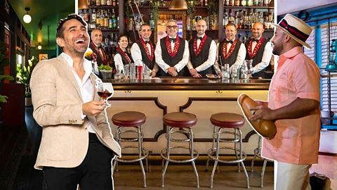 Giovanny Gutierrez holding a glass next to a Cuban musician, in front of a row of bartenders behind a bar counter (Credit: Javier Hirschfeld)