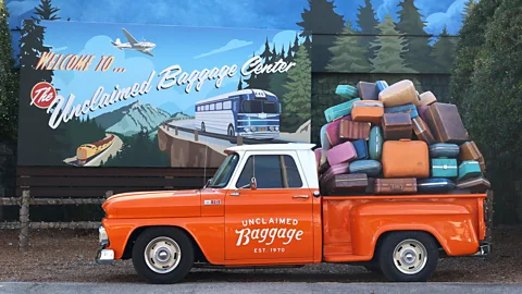 A sign that says Welcome to Unclaimed Baggage with an orange truck and piles of suitcases in the back of it (Credit: Jessica Parrillo)