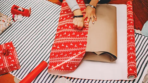 A person trying to pull red festive wrapping paper over an awkwardly shaped gift (Credit: Getty Images)