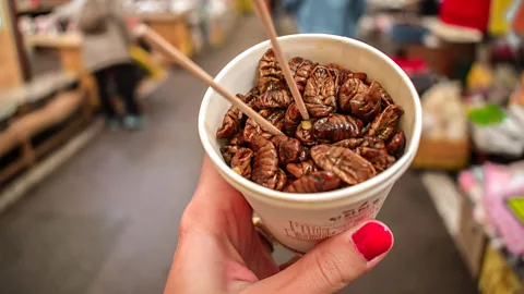 A paper cup filled with fried silk worms and chopsticks (Credit: Alamy)
