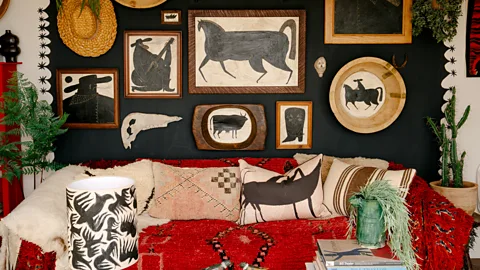 A red sofa with decorative pillows and artwork of animals hung on the wall behind (Credit: Imogen Rosemary/ Tabby Booth artist)