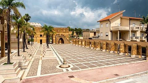 An empty tiled piazza in Gibellina, Sicily, bordered by low stone walls and palm trees (Credit: Getty Images)