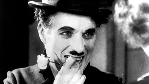 A close up of Charlie Chaplin smiling and holding a flower in City Lights (Credit: Alamy)
