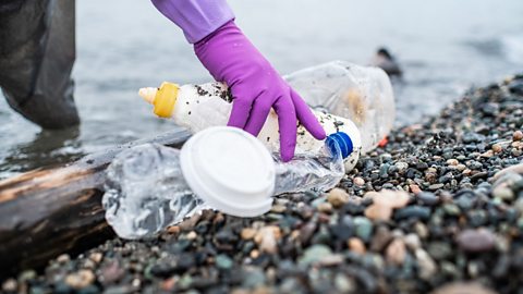 A gloved hand picking up plastic litter on a beach