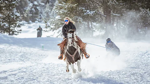 A skier grips a tow rope as a horse gallops across a snowy course during a skijoring race in Colorado (Credit: Keely Jackson)
