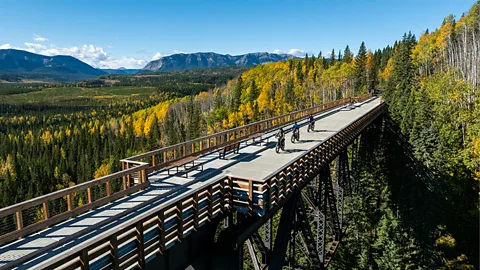 A scenic view of people cycling or walking across a historic railway trestle above a deciduous forest (Credit: Peter O'Hara/ Travel Alberta)