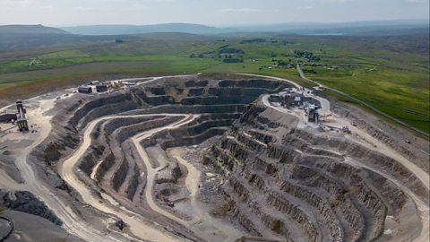 An aerial view of a large quarry. Site machinery is on the surface level and roads down into the depth of it can be seen. It has 7 levels at it's deepest.