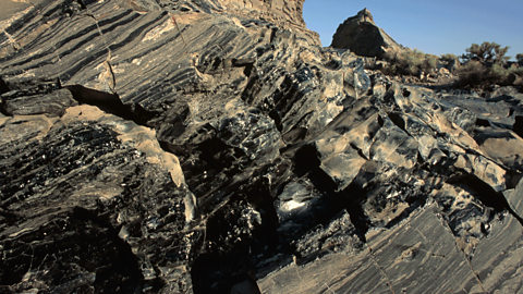Obsidian rock - a shiny, black, glass-like rock consisting of sharp, fractured reflective surfaces.
