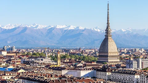 Turin's city skyline with the Mole Antonelliana rising above historic rooftops, with the Alps in the background (Credit: Getty Images)