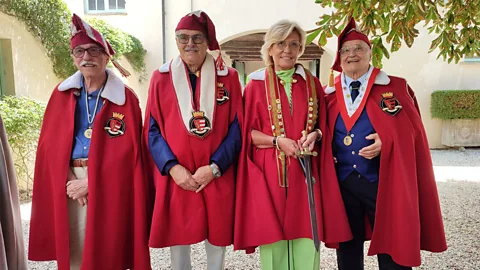 Four members of an Italian culinary confraternity stand side by side outdoors, wearing red ceremonial cloaks and medallions (Credit: Andrea Ivaldi di Gavi)