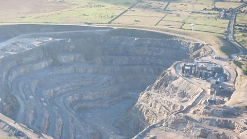 An aerial view of a deep quarry with some surrounding fields and roads. An earth bund can be seen around the top of Coldstones Limestone Quarry, Pateley Bridge, Yorkshire.