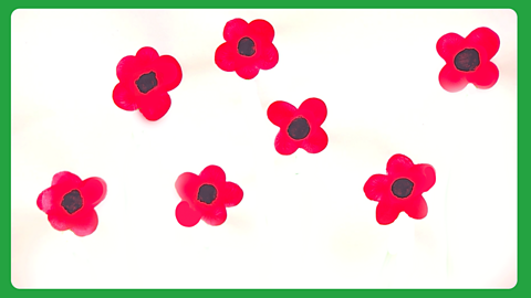 A white piece of paper with red painted petals on and black dots in the middle