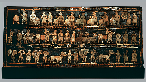 A decorated wooden box from ancient Sumer, shown from the side. One panel shows a king standing above soldiers and chariots in battle. The other panel shows the king sitting at a feast while people bring food and play music. The pictures are made from colourful pieces of shell and stone.